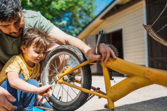 Father assisting son repairing old bicycle in back yard