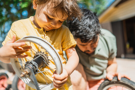 Boy holding wheel rim and repairing bicycle with father in back yard