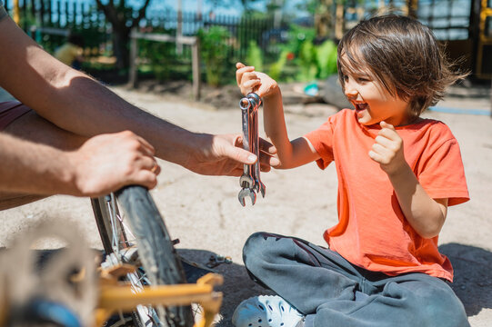 Happy boy sitting and giving wrenches to father in back yard