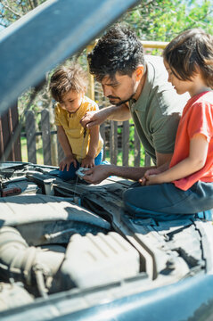 Father checking oil level of car with sons sitting on hood