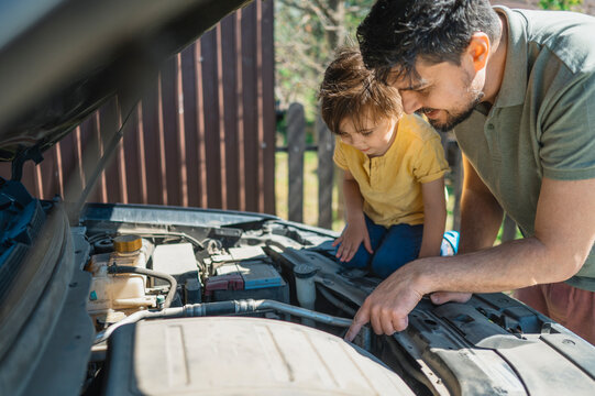 Happy father examining car engine with son sitting on hood in back yard
