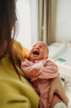 Mother holding crying baby girl in arms at home