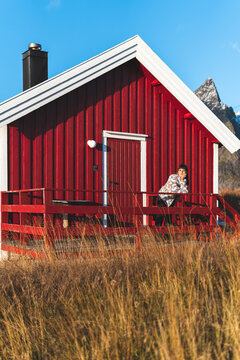Woman leaning on railing in front of red log cabin