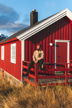 Thoughtful man sitting on railing of porch at red log cabin