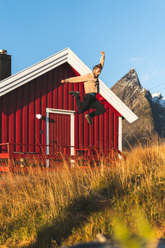 Carefree man jumping from railing in front of log cabin