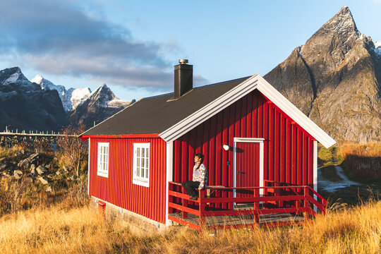 Woman sitting on railing of red log cabin near mountains