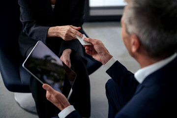 Business colleagues exchanging card sitting at office