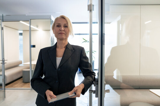 Businesswoman holding tablet PC and leaning on door at office - Powered by Adobe