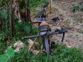 A rusty motorcycle with a makeshift wooden frame stands abandoned in a lush jungle clearing.