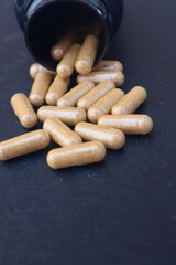 Brown capsule pills falling from its black bottle with close up view.