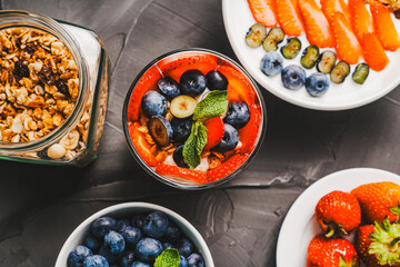 Dessert of strawberries and blueberries, granola and yogurt, cottage cheese and cream. A delicate parfait for a healthy breakfast in a white bowl and a glass glass with mint. Selected focus.