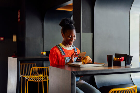 Smiling woman using smart phone in fast food restaurant