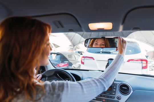 Redhead woman adjusting rear-view mirror in car - Powered by Adobe