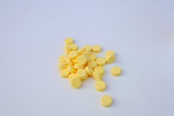 Yellow medicine tablets or vitamin C medicine are stacked on top of each other on a white background.