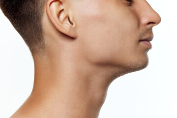 Close-up of a man's profile, focusing on his ear, jawline, and neck against white studio...