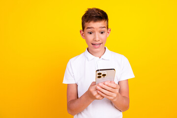 Photo of excited school boy wear white t-shirt getting likes modern device emtpy space isolated yellow color background