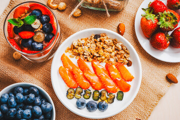 Granola with strawberries, blueberries and Greek yogurt in a white bowl and berry parfait on a wooden table with berries. A healthy dessert or breakfast.