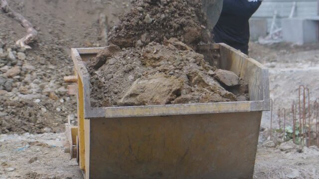 Godet de pelleteuse qui vide de la terre dans une grande benne. Excavator bucket that empties soil into a large bucket.