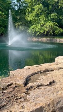 Erupting pond fountain trees boulders reflections daytime natural landscape