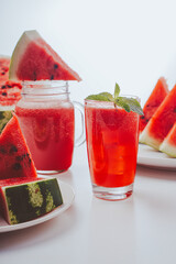 Refreshing watermelon freshly squeezed juice or smoothie with mint and lemon and sliced watermelon in bokeh on a light background. Selected focus