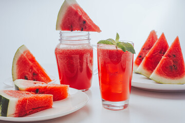 Refreshing watermelon freshly squeezed juice or smoothie with mint and lemon and sliced watermelon in bokeh on a light background. Selected focus