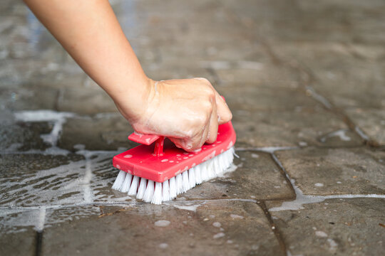 Action of janitor hand is using a scrub brush to scrubbing on granite rock floor. Home service job and hard working scene. Close-up with selective focus at the object.