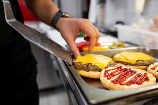 Close-up of a hand placing cheese slices on burger patties with ketchup in a kitchen setting, showcasing the food preparation process. Ideal for culinary, cooking, and fast food themes.