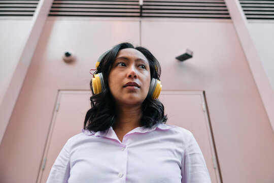 Serious businesswoman with bluetooth headphones near wall