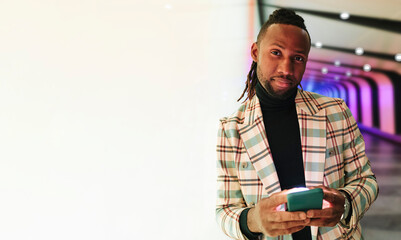 Businessman holding smart phone leaning on illuminated wall