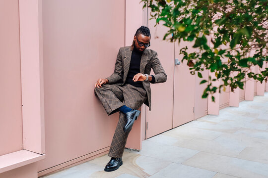 Businessman checking time and sitting near pink building