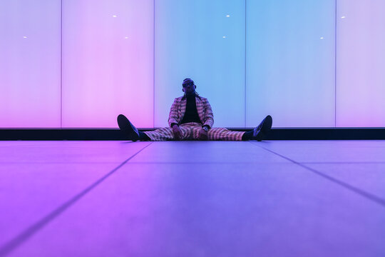 Businessman sitting with spread legs near illuminated wall