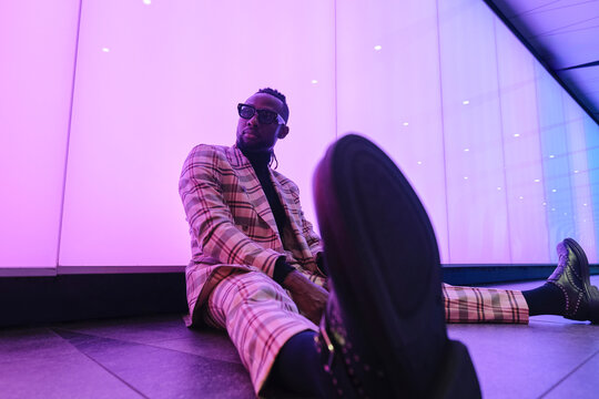 Fashionable businessman sitting near illuminated wall