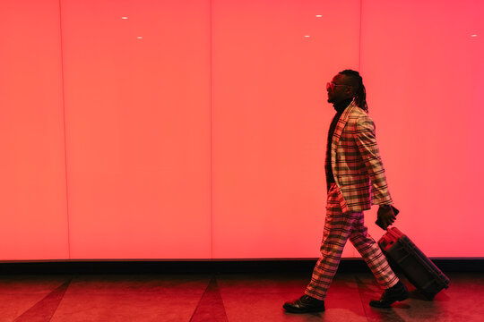 Businessman with luggage walking across red illuminated wall