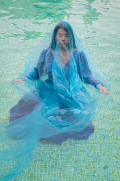 asian woman in a blue dress emerged in blue water pf swimming pool in art portrait