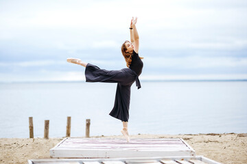 Graceful woman in arabesque position standing near lake