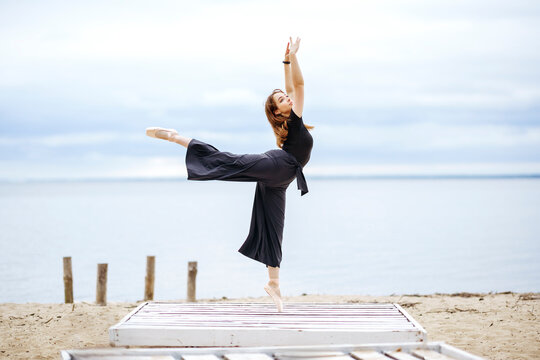 Graceful woman in arabesque position standing near lake