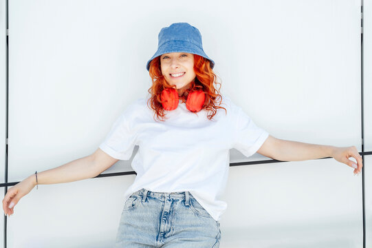 Smiling woman wearing bucket hat leaning on white wall