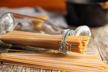 Uncooked whole grain pasta. Raw spaghetti in jar on wooden table.
