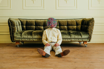 Man with mask of chaotic thoughts relaxing near sofa