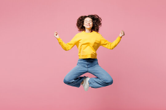 Full body young shocked surprised woman wearing yellow sweatshirt casual clothes jump high spread hands look camera isolated on plain pastel light pink background studio portrait. Lifestyle concept.