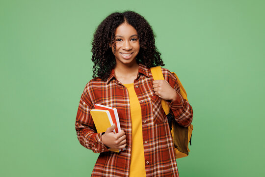 Young smiling happy cheerful smart freshman teen girl student wear brown yellow casual clothes backpack bag hold books isolated on plain green color background. High school university college concept.