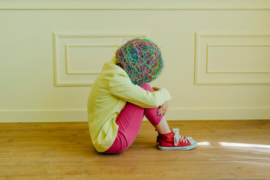 Woman with mask of chaotic thoughts sitting near yellow wall