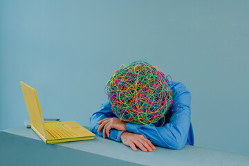 Tired businessman with mask of chaotic thoughts resting head on arms against blue background