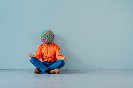 Businessman with mask of chaotic thoughts meditating near blue wall