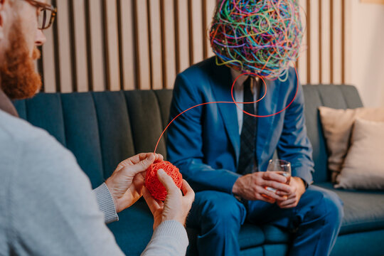 Psychotherapist untangling wire from chaotic mask of patient sitting on office