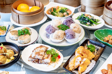 Image of various Chinese dim sum in a bamboo steamer, equipped with chopsticks and tea, on a wooden table. 
