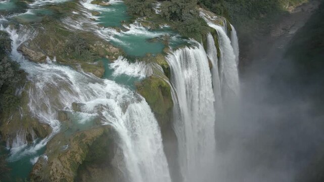 Aerial orbit around top of cascading water with mist rising in canyon from Tamul Waterfall Mexico