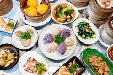 Image of various Chinese dim sum in a bamboo steamer, equipped with chopsticks and tea, on a wooden table. 