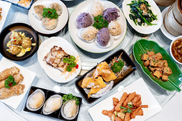 Image of various Chinese dim sum in a bamboo steamer, equipped with chopsticks and tea, on a wooden table. 