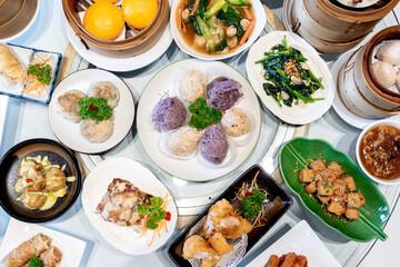 Image of various Chinese dim sum in a bamboo steamer, equipped with chopsticks and tea, on a wooden table. 